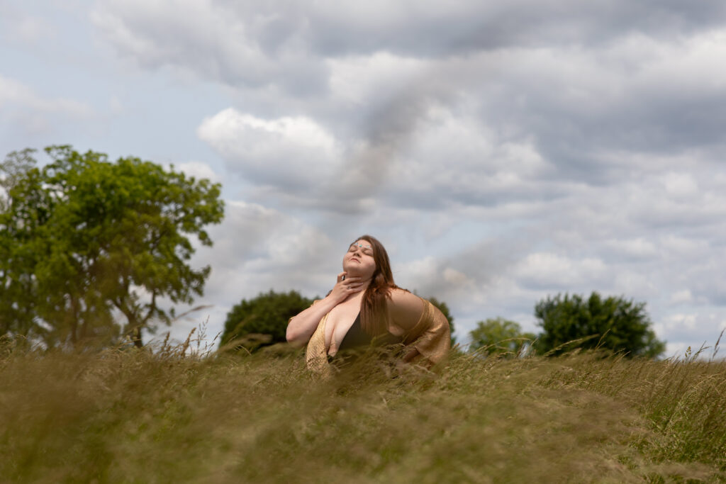 Woman kneeling in a golden field, hand on neck, eyes closed, embracing the moment during a natural light boudoir session in York, PA. Step Into the Sun: Outdoor Boudoir Photography in York, PA