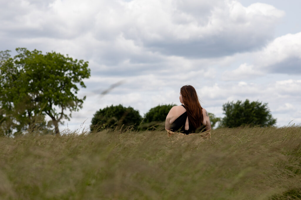 Back view of a woman in a field, facing the horizon, capturing the peaceful and reflective side of outdoor boudoir photography.